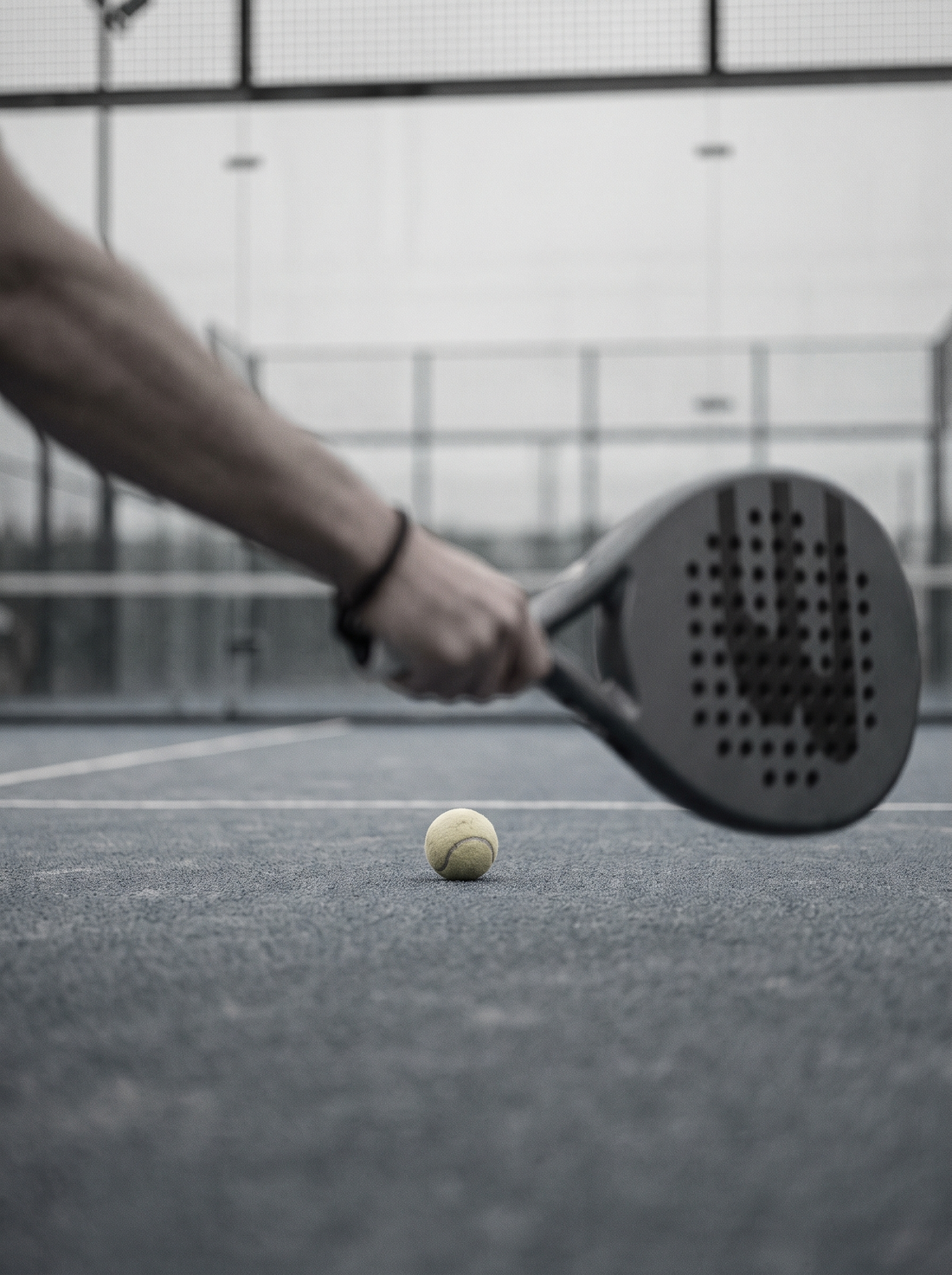 Lengan pemain dan raket padel setinggi net dalam gerakan kabur