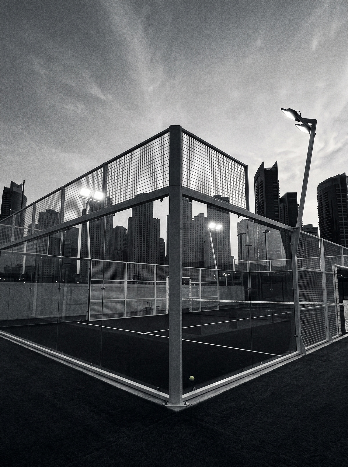 Lapangan padel berdinding kaca dengan latar gedung tinggi saat senja